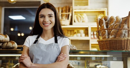 Pretty female baker in glasses scrolling and taping on the tablet computer while standing at the counter in the shop. Indoor