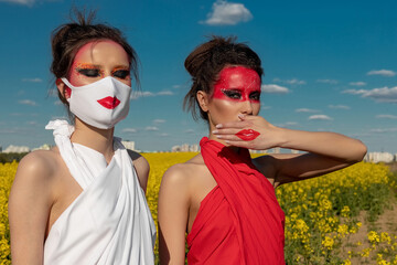 Two beautiful young brunette girls with creative bright makeup in tunics against a blue sky in a...