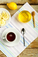 White cup with tea with lemon and honey on a table on a napkin.