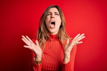 Young beautiful brunette woman wearing casual turtleneck sweater over red background celebrating mad and crazy for success with arms raised and closed eyes screaming excited. Winner concept