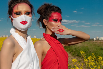 Two beautiful young brunette girls with creative bright makeup in tunics against a blue sky in a...