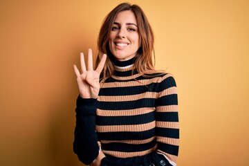 Young beautiful brunette woman wearing striped turtleneck sweater over yellow background showing and pointing up with fingers number four while smiling confident and happy.