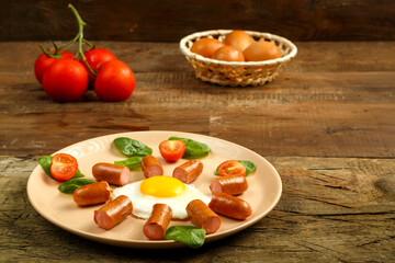 Fried eggs with sausages in the shape of a sun. Children's breakfast next to eggs and tomatoes.