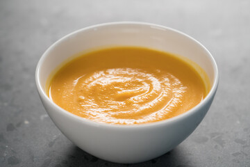 Pumpkin spicy soup puree in white bowl on concrete background