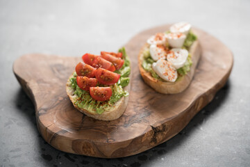 Bruschettas with avocado, tomato and mozzarella on wood board on concrete bacground