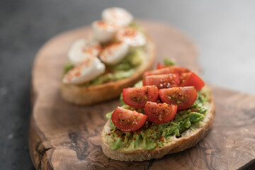 Bruschettas with avocado, tomato and mozzarella on wood board on concrete bacground