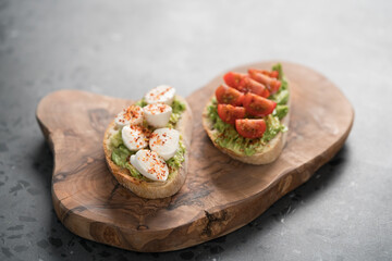 Bruschettas with avocado, tomato and mozzarella on wood board on concrete bacground