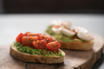 Bruschettas with avocado, tomato and mozzarella on wood board on concrete bacground