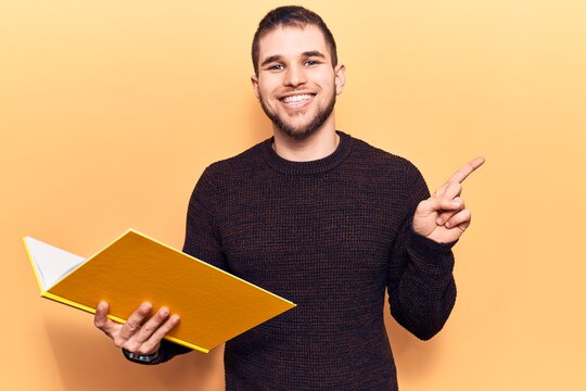Young handsome man reading book smiling happy pointing with hand and finger to the side