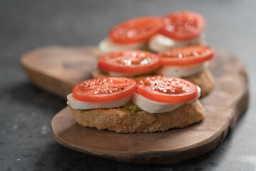 Bruschetta with tomatoes, mozzarella and pesto on olive wood board