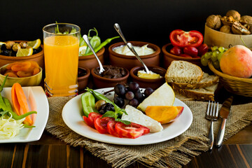 Fototapeta na wymiar Meatless and Eggless Breakfast with fresh fruits,cheese,olives,dry fruits,fresh orange juice,whole wheat bread and fresh vegetables on the wooden table.