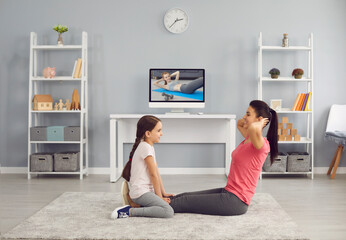 Happy mother and daughter working out together to video tutorial on TV at home. Cheerful family exercising indoors online - obrazy, fototapety, plakaty