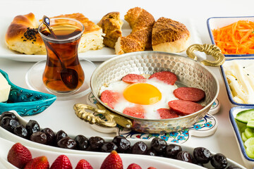 Traditional Turkish Breakfast with olives,cheese,salad,strawberries,pastry and egg with sausage in copper egg pan on the white surface.