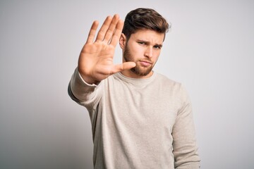 Young handsome blond man with beard and blue eyes wearing casual sweater doing stop sing with palm of the hand. Warning expression with negative and serious gesture on the face.