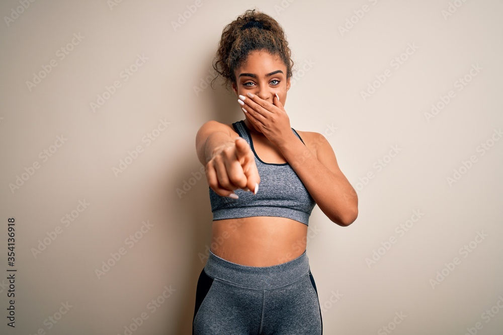 Poster Young african american sportswoman doing sport wearing sportswear over white background laughing at you, pointing finger to the camera with hand over mouth, shame expression