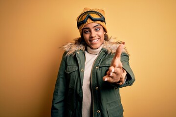 Young african american afro skier girl wearing snow sportswear and ski goggles smiling cheerful offering palm hand giving assistance and acceptance.