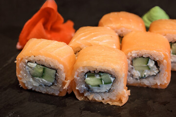 Close up view of philadelphia rice rolls, maki made of pink salmon, rice, cream cheese, cucumber served with wasabi and ginger on the black background.