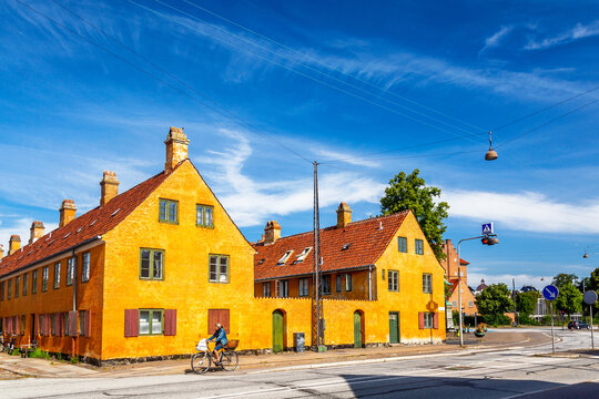 Old yellow houses of Nyboder district and woman on a bicycle during summer sunny day. Old Medieval district in Copenhagen, Denmark