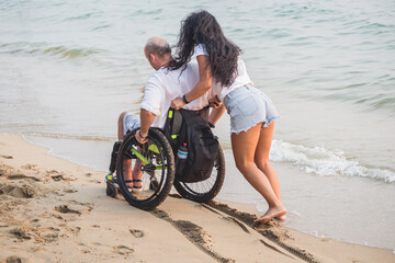 Disabled man in a wheelchair with his wife on the beach.