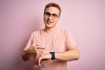 Young handsome redhead man wearing casual t-shirt standing over isolated pink background In hurry...