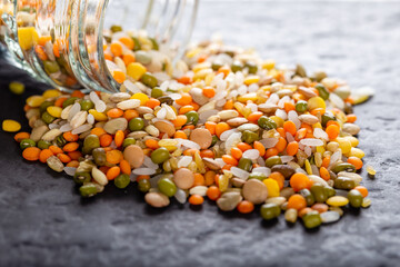 Colorful assorted lentils and whole grains seeds poured from a glass jar on the table