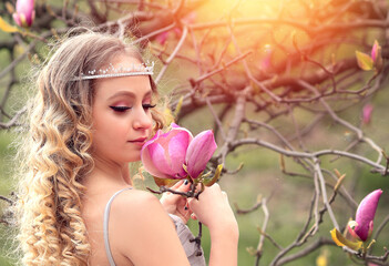 Obraz na płótnie Canvas Portrait of stunning young beauty blonde with pink magnolia close-up, Beauty blonde with jewelry for hair. Crystal decoration for women. Copy space. Sunset, bokeh effect. Flowers and floristry concept