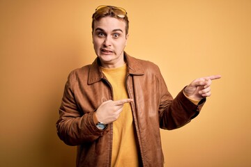 Young handsome redhead man wearing casual leather jacket over isolated yellow background Pointing...