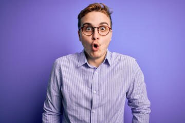 Young handsome redhead man wearing casual shirt and glasses over purple background afraid and shocked with surprise expression, fear and excited face.