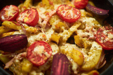 Cooked potato, baked with tomatoes, bacon and cheese in a pan.