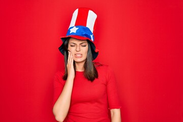 Young beautiful brunette woman wearing united states hat celebrating independence day touching mouth with hand with painful expression because of toothache or dental illness on teeth. Dentist