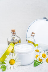 Obraz na płótnie Canvas Herbal cosmetic body cream in opened container, natural oil, fresh chamomile flowers, mirror on a white background. Natural organic moisturizer skincare product. Selective focus. Vertical. Copy space.