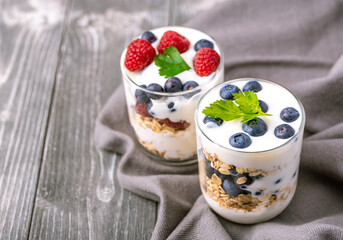 White yogurt in glass jar with blueberries on grey background.