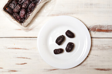 Dates on a plate on a light wooden background.