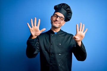 Young handsome chef man wearing cooker uniform and hat over isolated blue background showing and...
