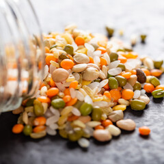 Colorful assorted lentils and whole grains seeds poured from a glass jar on the table