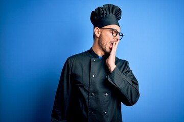 Young handsome chef man wearing cooker uniform and hat over isolated blue background bored yawning tired covering mouth with hand. Restless and sleepiness.