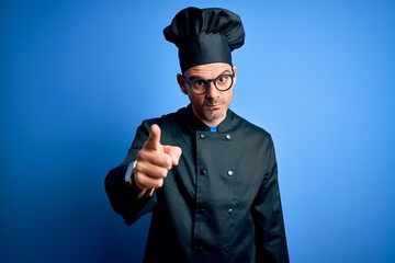 Young handsome chef man wearing cooker uniform and hat over isolated blue background pointing displeased and frustrated to the camera, angry and furious with you
