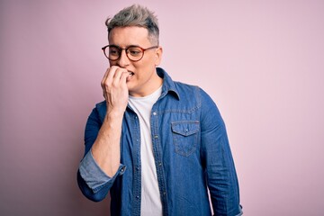 Young handsome modern man wearing glasses and denim jacket over pink isolated background looking stressed and nervous with hands on mouth biting nails. Anxiety problem.