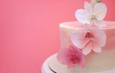 Obraz na płótnie Canvas Cake decorated with sugar flowers orchids close-up. Pink marble cake stands on a round white stand on a pink background. Beautiful dessert decorated with flowers.