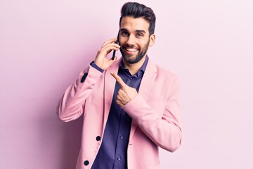 Young handsome man with beard having conversation talking on the smartphone smiling happy pointing with hand and finger