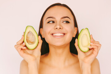 Portrait young happy brunette woman posing with avocado slices, isolated on white background. Beautiful funny girl with perfect clean skin hold green avocado in hands. Beauty treatment, dieting, detox
