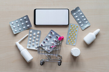 Online pharmacy. Smartphone app for buying medicine. Top view of a mini shopping trolley with tablet blisters and a telephone.