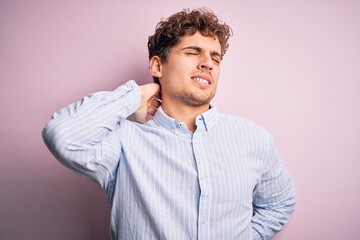 Young blond handsome man with curly hair wearing striped shirt over white background Suffering of neck ache injury, touching neck with hand, muscular pain