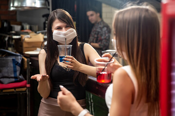 girls in medical masks chatting in a pub. girls in medical masks are talking at the bar. girls in medical masks drink cocktails