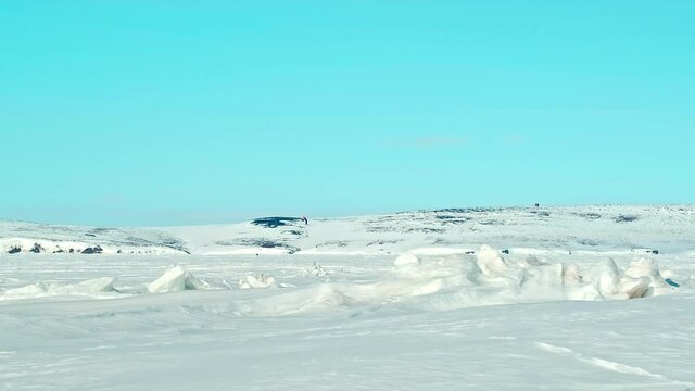 distant snow surfer with parachute silhouette on endless frozen sea with ice hummocks under clear blue sky on sunny day