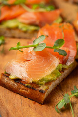 bruschetta with trout or salmon and avocado on a wooden board decorated with microgreens