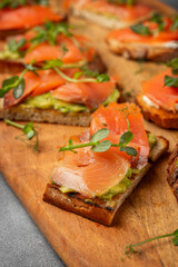 bruschetta with trout or salmon and avocado on a wooden board decorated with microgreens