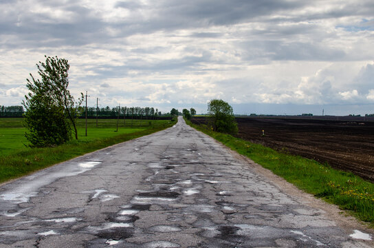 Broken road with puddles full of water. A day for the construction of the road was stolen. Corruption in the country