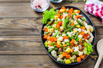 Sauteed vegetables, beans, cauliflower, carrot, pumpkin  in cast iron skillet on wooden background.