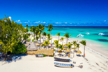 Aerial drone view of beautiful atlantic tropical beach with palms, straw umbrellas and boats. Bavaro, Punta Cana, Dominican Republic. Vacation background. - obrazy, fototapety, plakaty